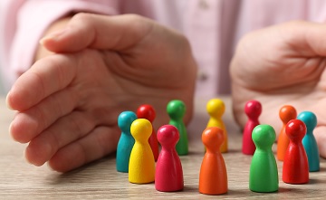 Zwei Hände umschließen schützend eine Gruppe bunter Spielfiguren – Sinnbild für Betreuung, Schutz und Gemeinschaft in besonderen Wohnformen.